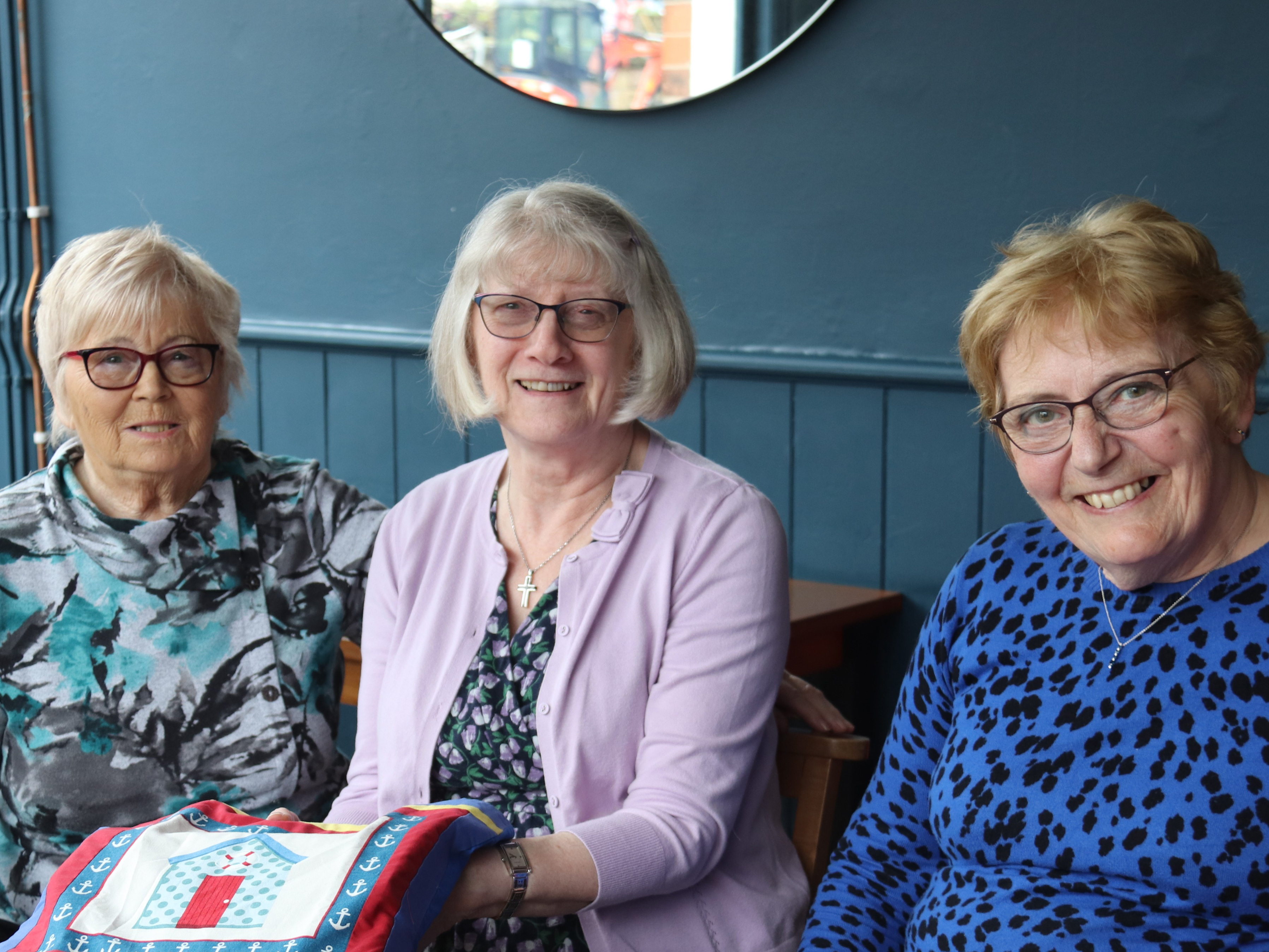 Three smiling people sat a table in a cafe